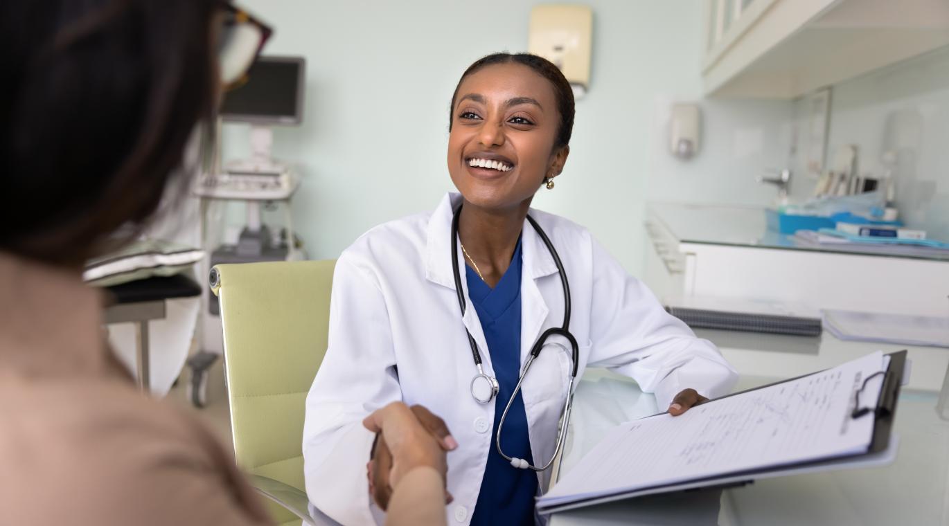 Happy young medical practitioner woman finishing consultation with handshake, shaking hand with grateful female patient