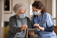 nurse talking to elderly patient at home with masks on