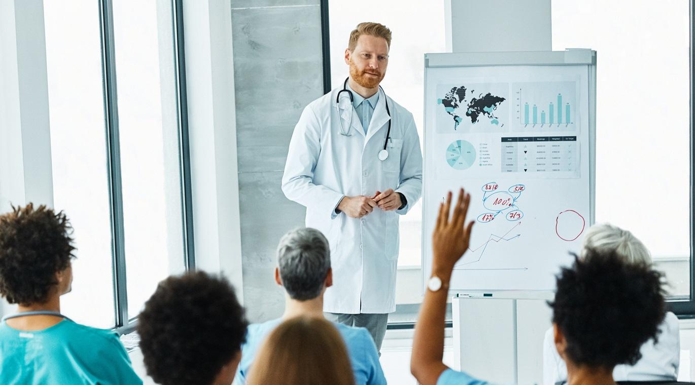 male physician presenting to a group of physicians at the front of the room