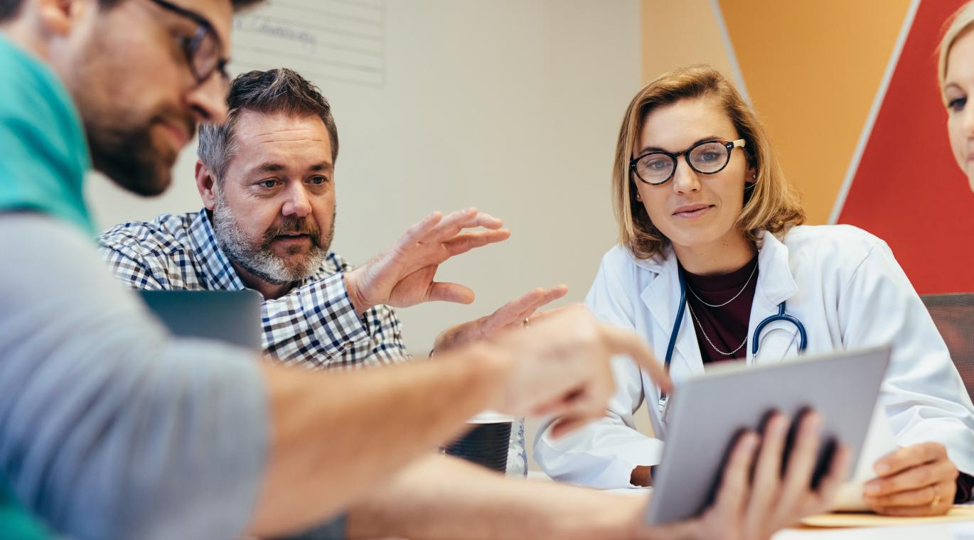 physician with patients at a table looking at a tablet