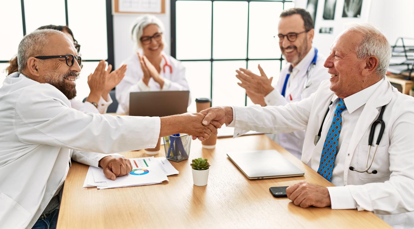 two physicians shaking hands across a table