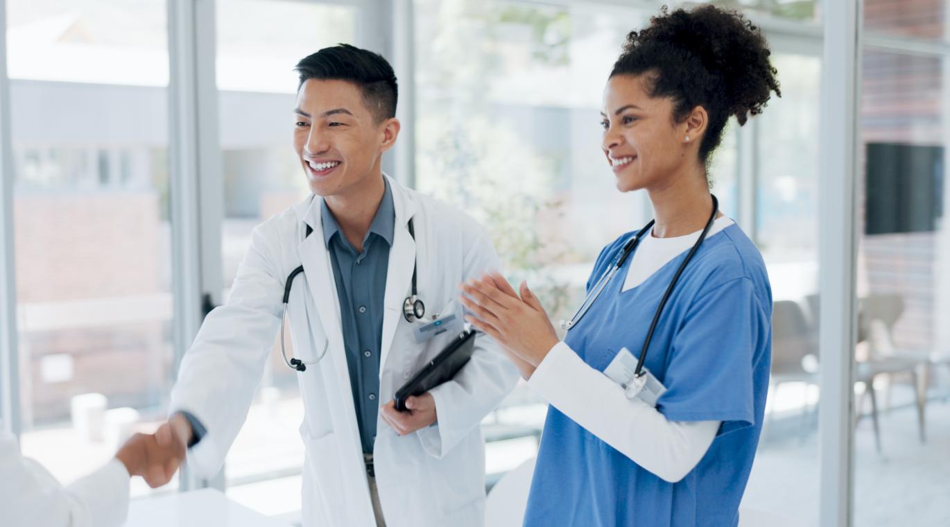 Two physicians smiling and one is shaking hands with a physician out of the picture