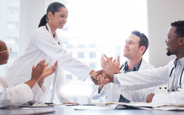 a group of doctors applauding as a new team member is welcomed aboard during a meeting.